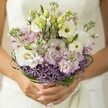 This tender composition captures the delicate interplay of colour, texture, and emotion embodied in a bridal bouquet, lovingly arranged for a spring or summer celebration in Epping. Creamy white Lisianthus unfurl their papery, ruffled petals, surrounded by clouds of light pink and soft lavender stock flowers-a palette reminiscent of sunrise over Epping Forest on a peaceful morning. Bold, star-like purple Allium at the base provides whimsical contrast, lending a subtle modern edge to the rounded, romantic forms above. Elegant, looping strands of deep green bear grass encircle the arrangement, giving it polished structure and drawing the eye through layers of bloom and leaf. The bride's hands, neat nails aglow with blush polish, cradle the bouquet in a gesture of anticipation and joy. The softly blurred backdrop of an ivory wedding gown evokes the understated grace of celebrations held in Epping's historic churches and pretty countryside venues. With every petal, the bouquet whispers stories of love and local pride-fragrant and fresh, crafted just for a lifetime moment. Whether destined for a grand reception or an intimate garden ceremony, this arrangement reflects the artistry and care found in every creation from Flowers Epping.