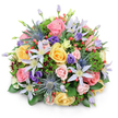 A lush, domed bouquet photographed against a pure white background, its soft shadow giving the arrangement a gentle three-dimensional presence. The composition is densely packed and hand-tied in a classic rounded silhouette, where soft pink, buttery yellow, and creamy peach garden roses unfurl in layered spirals and sit at varying stages of bloom, lending a romantic, tactile heart to the design. Threaded through those roses are star-shaped clematis in pale lavender and white, their open petals and sunny yellow centers reaching outward like small beacons of light. Architectural contrast comes from metallic-blue Eryngium (sea holly) thistles, their spiky, globe-like heads introducing a modern, almost coastal edge against the softer petals. Nestled among the larger forms are deeper purple lisianthus-some tight and ruffled, others easing open-and glossy clusters of red Hypericum berries that catch the eye with bright, juicy punctuation. A varied palette of foliage underpins the bouquet: broad glossy leaves for structure, feathery sprigs that breathe softness into the dome, and hints of dark burgundy filler foliage that deepen the overall tone. The scent suggests a fresh garden after a light shower-sweet rose perfume with green, leafy undertones-and the overall mood leans toward celebration, warm thanks, or an elegant centerpiece. As a local florist in Epping might say, this arrangement evokes walks through Epping Forest in early summer, where cultivated blooms meet wild textures; it's equally suited to a birthday table, anniversary gift, or a thoughtful gesture delivered from your neighbourhood shop to nearby Bell Common or the High Street.