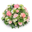 A soft, dome-shaped floral tribute composed of densely packed blush pink roses and clusters of pure white freesia, presented against a clean white background. The arrangement reads like a gentle pillow of blossoms: classic full pink roses in varying sizes - from large, velvety blooms with petals unfurling in concentric swirls to smaller spray roses that add a delicate, textured rhythm. Bright white freesia punctuates the roses with upright sprays and bell-shaped blooms; some freesia are fully open, their pale corolla revealing a faint yellow stamen, while others hold as tight buds ready to unfurl. Rich, glossy greens cradle the flowers and create depth - broad dark leaves such as ruscus or salal form the base, while smaller, cream-edged variegated leaves (likely Pittosporum) lift the palette and add a subtle, elegant contrast. No stems are visible, giving the piece a refined, formal silhouette that casts a soft shadow on the white surface beneath. Natural light gently models each petal and leaf, highlighting textures from the satiny rose petals to the crisp freesia buds and the slightly waxy shine of the foliage. The overall mood is peaceful and consoling; this is a calming design suited to memorial services, bedside sympathy, or a thoughtful gift that offers quiet comfort. As a local florist who often prepares tributes for services near Epping High Street and the tranquil edges of Epping Forest, I imagine this arrangement placed on a chapel table or a reception desk, where its gentle colours and fresh scent offer solace and understated beauty.
