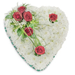 A solemn, heart-shaped memorial spray composed entirely of small, pristine white chrysanthemums sits against a clean white background, its surface dense and cushion-like and inviting touch. The chrysanthemums are arranged so closely their rounded heads create a seamless, cloud-soft bed whose cool white hue reads as purity and calm; from this white expanse a careful diagonal sweep of deep red roses rises from the upper left, the roses' velvety petals fully opened and saturated with a rich crimson that reads as love, respect and sorrow. That primary cluster of three roses is tucked among glossy broad leaves, airy fern-like fronds and a few slender arching blades of bright green bear grass, which extend outward like quiet brushstrokes to give movement and a living rhythm across the heart. Two solitary red roses interrupt the white field-one near the top right curve and one at the lower point-each paired with a small fan of greenery that cradles the bloom and creates balance. A narrow emerald-green satin ribbon trims the heart's edge, providing a refined frame and a subtle, dignified contrast to the white cushion. The arrangement is lit from above so delicate shadows fall between the chrysanthemum heads, revealing depth and the meticulous craftsmanship of a florist's hand. The scent is soft-honeyed chrysanthemum warmth underscored by the deeper perfume of the roses-conveying a quiet, respectful presence. This traditional funeral heart, often chosen for services at local parish churches or graveside in the Epping area and for private memorials, expresses enduring affection, gentle solace and composed remembrance without flourish.