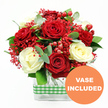 This photograph presents a rich, romantic bouquet of red and white roses, designed in a style that would feel at home in many Epping living rooms and dining spaces. The main focus is on the large, fully opened blooms: deep, velvety red roses sit shoulder to shoulder with soft, creamy white roses, their petals layered in spirals that curl gently at the edges. Nestled among them are clouds of tiny bright red filler blossoms, echoing the look of tinted baby's breath and giving the arrangement a light, almost frosted texture, as though the flowers were dusted with festive colour. Round clusters of glossy red hypericum berries peek through the petals, adding warmth and a sense of abundance. Lush greenery surrounds and supports the central blooms; broad green leaves mix with slender, slightly bluish eucalyptus sprigs, whose cool tone provides a modern counterpoint to the rich reds. All of this is carefully arranged in a clear, rectangular glass vase, where the straight, trimmed stems are visible and orderly. Around the midsection of the vase, a green and white gingham ribbon wraps neatly, lending a touch of rustic charm that recalls country homes around Epping and quiet lanes leading toward the forest. In the lower right corner of the image, a bright orange circular icon stands out, clearly marked with the words VASE INCLUDED in white capital letters. The overall impression is of a thoughtful, ready-made floral gift, ideal for same-day delivery across Epping for anniversaries, Valentine's Day, winter celebrations, or simply to bring a feeling of warmth and care into someone's home.