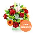 The photograph shows a joyful, modern mixed bouquet that looks ready to be placed on a dining table in Epping after a visit from the local florist. At its core are lush, velvety deep red roses, their petals tightly layered and slightly curled at the edges, paired with softly ruffled red-orange carnations that bring a sense of fullness and warmth. Bright orange gerbera daisies, each with a striking dark central disk, sit proudly among the other flowers, their flat, daisy-like petals radiating outwards like bright sunbursts on a clear afternoon. Nestled between these bolder blooms are small, spherical lime-green pompom chrysanthemums, adding playful pops of fresh green that echo the foliage of Epping's surrounding countryside. Rising above the main cluster, white Oriental lilies add height and elegance; some are fully open, their star-shaped petals marked with delicate pink stripes and tipped with dusty stamens, while others remain as smooth, elongated buds waiting to open. The arrangement is cradled in a clear, rectangular glass vase that reveals the criss-cross of stems below, and a light green and white gingham ribbon wraps around the base like a decorative band, giving the design a relaxed, rustic charm suitable for homes from Coopersale to Ivy Chimneys. Rich green leaves and sprigs of silvery eucalyptus weave through the bouquet, adding texture, depth, and a hint of soft, herbal fragrance. In the lower right corner of the image, a circular orange badge overlaps the vase, with the words VASE INCLUDED printed in bold white capital letters, clearly indicating that this bright, celebratory display arrives complete and ready to enjoy anywhere in Epping.