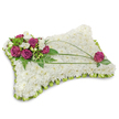 A rectangular pillow-shaped sympathy tribute, photographed on a clean white background with a soft shadow beneath, shows a densely packed bed of pristine white chrysanthemums that form a cloudlike, textured surface. The tiny chrysanthemum florets sit closely together to create the impression of a plush, restful cushion; their compact petals read as softness to the touch and purity to the eye. At the upper left a concentrated cluster of deep magenta or fuchsia roses provides a striking focal point - velvety blooms opening in layered spirals - interspersed with small white freesia or lisianthus that add delicate, fragrant highlights and a sense of lightness. Rich emerald-green foliage and feathery fern fronds cradle the primary cluster, giving natural depth and a fresh contrast against the white body of the pillow. Across the face of the cushion, two or three long, arching blades of bright green bear grass or similar linear foliage sweep diagonally, creating a graceful line that draws the eye from the floral cluster toward the opposite corner. Near the lower right a single matching fuchsia rose is placed thoughtfully among a few leaves, balancing the composition and echoing the main accent. The edge of the pillow is neatly finished with folded lime-green satin ribbon, forming a subtle scalloped trim that frames the tribute and introduces a gentle colour boundary. The overall mood is one of quiet consolation and peaceful remembrance: clean light, soft textures, and a composition designed to convey respect and solace at funerals or memorial services in the Epping area, reflecting traditional bereavement floristry with attentive craftsmanship.