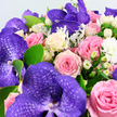In this detailed close-up, a sumptuous bouquet seems to spill towards the viewer, echoing the kind of statement arrangement you might see prepared for a special event in one of Epping's elegant homes. Dominating the composition are several large Vanda orchids, their petals a deep, luxurious purple marked with a striking, darker net-like pattern that looks almost like fine lace laid over velvet. Surrounding these exotic stars is a generous collection of roses in soft, flattering tones: gentle blush pinks, medium rose shades, and creamy whites that sometimes blush into the faintest pale yellow at the centres. The roses vary from tight, rounded buds to open, spiralled blooms, each petal smooth and luminous in the light. Nestled among them are clusters of small, round white Hypericum berries, their glossy skins creating a pleasing contrast with the softness of the petals. Dotted throughout are tiny white filler flowers, like miniature chrysanthemums or carnations, that lend a feathery fullness and help blend the colours seamlessly. Bright green, oval foliage gives structure and freshness, while hints of silver-green, velvety leaves-similar to Dusty Miller-provide a cool, airy softness that frames the richer tones. The bouquet fills almost the entire frame, set against a soft white background that enhances the colours without overpowering them. The overall mood is one of understated luxury and tender celebration, perfect for a romantic surprise delivered across Epping and nearby villages or as a centrepiece for an intimate dinner looking out towards Epping Forest. You can almost imagine leaning in to catch the gentle fragrance of roses and fresh greenery.