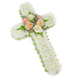 A traditional floral cross for a funeral or memorial is shown in close detail against a spotless white background, its simple shadow adding a gentle sense of depth as if the piece were resting on a table in a quiet Epping chapel. The cross itself is fully covered in small, button-like white chrysanthemums, each flower tightly nestled beside the next to create a thick, cushiony surface with no gaps or greenery breaking the snowy expanse. This continuous layer of white blooms suggests purity, peace, and a sense of tender care, as though each flower has been placed with a specific memory in mind. At the centre where the arms of the cross meet, a compact cluster of roses offers a soft contrast in colour and form. Open roses in blush pink, soft peach, and creamy white gather together, their rounded heads and layered petals giving a romantic, heartfelt touch. Fine fern fronds and tiny purple-lavender filler flowers weave between the rose blooms, adding airy texture and subtle movement to the focal point. Running all around the outer edge, a narrow lime green ribbon is carefully wrapped beneath the chrysanthemums, creating a slim, fresh border that gently defines the cross's outline, like a hint of new life against a field of white. The overall impression is one of quiet reverence and comfort, the kind of floral tribute families in and around Epping might choose to accompany a farewell at a local church or crematorium, expressing sympathy, faith, and lasting remembrance.