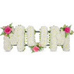 A heartfelt floral tribute spells out the word MUM in striking, upright letters, filling the centre of the image against a clean white background that highlights every bloom. Each letter is entirely blanketed with tiny white chrysanthemum flowers, the tight massing of petals creating a smooth, pillow-like finish that feels calm and reassuring. The flowers are supported by a discreet dark green framework and a neat ribbon trim along the base, offering both strength and a subtle line of colour that helps define the shape of each letter. Three carefully balanced bursts of pink and green bring softness and personality to the tribute. On the upper left corner of the first M, a rich fuchsia rose blooms fully, surrounded by smaller blush-pink spray roses and buds, framed by delicate fern fronds that arc gently like the fronds you might see in the gardens around Epping's quiet residential streets. Another similar grouping nestles in the bottom curve of the U, drawing focus to the centre and suggesting a heart of love and memories. The final cluster sits at the top right of the second M, mirroring the first and giving the arrangement a pleasing symmetry, as though the word is gently cradled in colour at each end. The fresh white and vivid pink tones, mixed with feathery greenery, evoke both tenderness and dignity-a fitting floral message for a much-loved mum. You can imagine this tribute resting on a casket in a local Epping chapel or laid carefully at a graveside, its gentle fragrance and thoughtful design offering comfort to friends and family gathered in remembrance.
