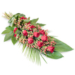 An elegant red rose funeral spray is displayed on a stark white background, the simplicity of the setting drawing all attention to the flowers and foliage. The arrangement lies diagonally, with the stems gathered at the upper left and the blooms flowing down towards the lower right, forming a gentle, elongated teardrop shape often chosen for meaningful farewells in the Epping area. Luxurious red roses dominate the design, their velvety petals ranging from tightly closed buds to fully opened blossoms that reveal intricate layers at the heart of each flower. The roses are interspersed with rounded clusters of pinkish-red Hypericum berries, which add a more delicate, almost pearly texture alongside the rich petals, softening the deep red with a subtle blush. Beneath and around the flowers sits a solid base of lush, dark green leaves, broad and glossy like Salal or Ruscus, overlapping to form a deep, verdant backdrop. From this base, fine, feather-like palm fronds and slender greenery fan gracefully outward, particularly at the lower right edge, giving the spray a sense of movement and natural flow. A neatly wrapped band of smooth green leaf secures the stems at the top left, creating a polished finish that reflects the steady hand of a skilled florist. Set against the clean white, the combination of rich red, fresh green, and gentle berry tones conveys a mood of quiet honour, love, and farewell, suitable for delivery to local chapels, homes, or cemeteries throughout Epping and the nearby countryside.