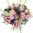 A richly romantic bouquet is set against a clean white background, its colours unfolding like a quiet love story told in flowers. At the centre, full garden roses in blush pink, dusty mauve, and antique rose curl open in soft spirals, exuding the calm elegance you might associate with a peaceful evening in Epping after a walk near the forest. Around them, ruffled carnations create a sense of softness and abundance; their petals fade from creamy blush at the heart to vivid fuchsia or plum along the edges, adding both texture and a gentle flicker of intensity. Threaded between these warmer tones, deep indigo and royal blue blooms-some closed in graceful, tulip-like buds, one an open anemone with a near-black centre-add dramatic contrast, like dashes of ink on a pastel page. Pale lavender and lilac stock stems rise among the larger flowers, each slender spike dotted with many tiny blossoms that lend airy height and the suggestion of a light, powdery scent. The bouquet is embraced by foliage: rounded, silvery-green eucalyptus discs mix with darker, glossy leaves, giving structure and a fresh, green aroma that balances the sweetness of the blooms. The hand-tied stems gather neatly at the base, a visible sign of careful, local craftsmanship, as if prepared moments ago in an Epping workshop for delivery to a home on Ivy Chimneys or a cosy café off the High Street. The overall feeling is tender and uplifting, perfectly suited to anniversaries, heartfelt birthdays, or simply letting someone in Epping know they are cherished.