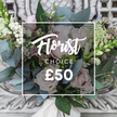 A hand-tied, garden-style bouquet resting on an antique cream console, captured in soft daylight that lets every texture breathe. Large, petal-soft blush roses form the heart of the arrangement, their unfurling heads suggesting quiet romance; they're punctuated by clusters of bright white berries - the round, glossy contrast of snowberries or hypericum - which lift the composition with playful highlights. Sprays of tiny white filler blooms, delicate as confetti, thread through the roses and mingle with smaller, deeper pink-to-burgundy florets that add a quiet depth. Dusty blue-green eucalyptus leaves fan around the blooms, their rounded shapes and faint silver bloom creating a cool, aromatic frame and a tactile contrast against the velvet petals. Taller, slender green-and-white spikes peek from the sides, providing gentle vertical movement and a natural, countryside rhythm. The stems are gathered and finished with a soft cream satin ribbon that trails slightly, reinforcing the bespoke, hand-crafted feel. Behind the bouquet, the ornate, distressed surface of the console and its carved details provide an elegant, timeless backdrop that's intentionally muted so the fresh colours pop. The overall mood is rustic-chic and comforting - as if the flowers were just gathered from a cottage patch near Epping Forest early on a slow morning and brought inside to brighten a hallway. This arrangement feels perfectly suited to a birthday, an anniversary, or a spontaneous act of kindness for someone in Epping or the surrounding villages, offering tactile contrast, fragrance from eucalyptus, and a composed but effortless beauty that reads as thoughtful and genuine to anyone unable to see it.