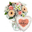 A joyful Mother's Day composition is set against a spotless white backdrop, giving the impression of a studio display carefully styled by a local Epping florist who understands how families in the area like to celebrate their mums. At the heart of the image sits a mixed bouquet in a clear, gently rounded glass vase, the stems visible inside like green brushstrokes in water. Around the neck of the vase, a simple strand of light brown twine is tied in a relaxed bow, adding rustic charm that suits homes from central Epping to the quieter roads near Coopersale. The floral arrangement is full and rounded, built from soft pastel tones that feel comforting and bright: peach-pink roses open wide, their layered petals spiralling outwards in velvety curls, while several peach gerbera daisies with dark, almost black centres bring a playful, daisy-like character. Between these feature blooms, airy sprays of white baby's breath create a cloud-like softness, and clusters of small white chrysanthemums with fresh green centres provide texture and a clean, garden-fresh look. Lush green foliage weaves through the blooms, anchoring the palette and suggesting the scent of a spring garden after rain in nearby Epping Forest. Just behind the flowers, a small white Mother's Day card nestles discreetly, its colourful message mostly hidden. To the right of the vase, a large heart-shaped Mylar balloon leans into the arrangement. Its white surface is sprinkled with shiny gold and silver confetti dots, and in the centre a peach heart holds the words HAPPY Mother's DAY written in contrasting black, with Mother's in an elegant, flowing script. Together, bouquet and balloon create a tender, celebratory gift, ideal for same-day delivery to mums across Epping and surrounding villages.