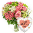A joyful Mother's Day bouquet and balloon pairing is shown against a crisp white background, reminiscent of a product shot taken in a quiet studio just off Epping High Street. The arrangement sits in a clear glass vase on the left, its stems visible through the water, while a heart-shaped foil balloon floats to the right, slightly lower than the flowers. The bouquet has a rounded, generous shape, filled to the brim with pastel pinks, lime greens, and bright whites. At the centre, a soft pink rose stands out as a focal point, its petals spiralling open with a gentle blush that suggests warmth and gratitude. Surrounding it are clusters of delicate pink spray-style blooms, similar to small carnations or Kalanchoe, offering a velvety, textured feel. Fluffy lime-green hydrangea-like florets or button chrysanthemums add volume and freshness, their rounded shapes echoing new spring growth around Epping Forest. Airy sprigs of white filler flowers, reminiscent of baby's breath or tiny daisy sprays, are threaded throughout, catching the light and adding a light, cloud-like softness. Darker green leaves peek from beneath the blossoms, framing the colours and anchoring the design so it feels lush yet balanced. To the bottom right, the shiny foil balloon adds a playful finishing touch. Its white background is scattered with irregular coral or peach-coloured confetti dots, mirroring the warmer tones in the bouquet. In the centre of the balloon, a larger solid coral heart carries the message HAPPY MOTHER'S DAY in an elegant dark script. Together, the fresh flowers and balloon convey a sense of celebration and appreciation, like a thoughtful surprise arriving at a family home somewhere in Epping on a bright spring morning.