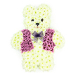 A softly expressive floral teddy bear sits in the centre of the image, carefully sculpted from countless creamy white chrysanthemums so close together they resemble a layer of plush fur. The rounded head, plump body, and slightly outstretched paws create a familiar, cuddly silhouette that brings to mind storytime and nursery shelves, transformed here into a tender memorial piece. Deep, dark flower centres form the bear's eyes and nose, adding definition and a hint of sparkle that makes the face appear kind and quietly reassuring. Over its chest, a charming vest has been created from rich purple and lilac blooms, their petals overlapping like tiny fabric folds, subtly shaped into panels and lapels for a dressed-up yet childlike look. Nestled at the neckline, a delicate lavender mesh bow ties the design together, its light, airy texture standing out against the dense, cushiony chrysanthemums. The scene is calm and uncluttered, with a pale backdrop that lets the cream and purple tones speak of gentleness, remembrance, and the enduring comfort of love. This type of tribute is often chosen by families in Epping and nearby villages such as Thornwood and North Weald to honour a young life or someone remembered as forever young at heart. Whether placed near the coffin, by a memory table at an Epping funeral home, or later at a graveside overlooking the edge of Epping Forest, this chrysanthemum teddy bear becomes a symbolic embrace, expressing sympathy, tenderness, and the hope that cherished memories will remain soft and close, like a beloved toy held in the arms.